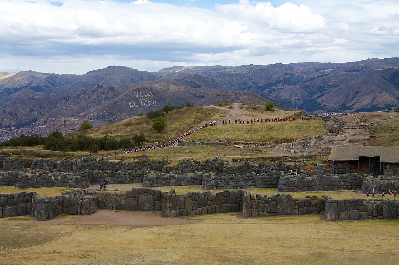 Personas vestidas con trajes tradicionales caminando en fila hacia la fortaleza de Sacsayhuamán durante la fiesta del Inti Raymi.